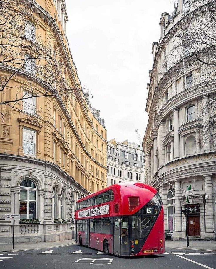 a red double decker bus driving down a street next to tall buildings in the city