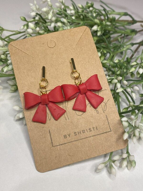 two red bows are hanging from the back of a pair of earrings on a card