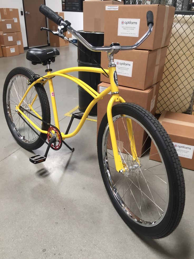 a yellow bicycle parked in a warehouse with boxes on the floor and behind it is a black seat