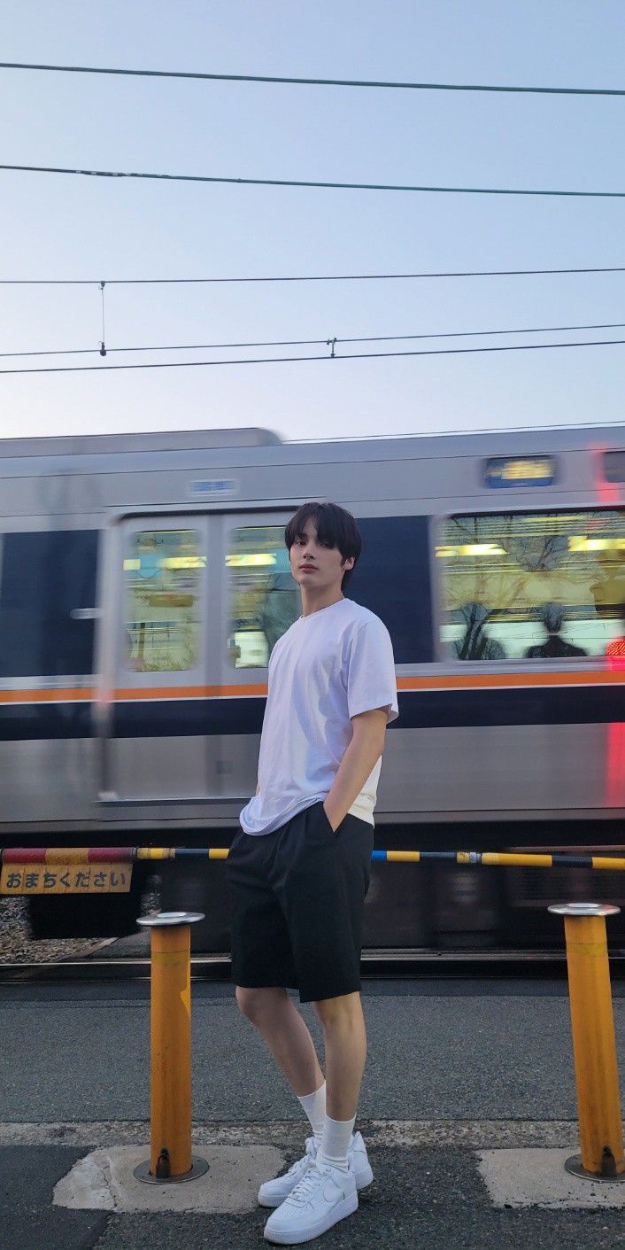 a young man standing on the side of a road next to a train passing by