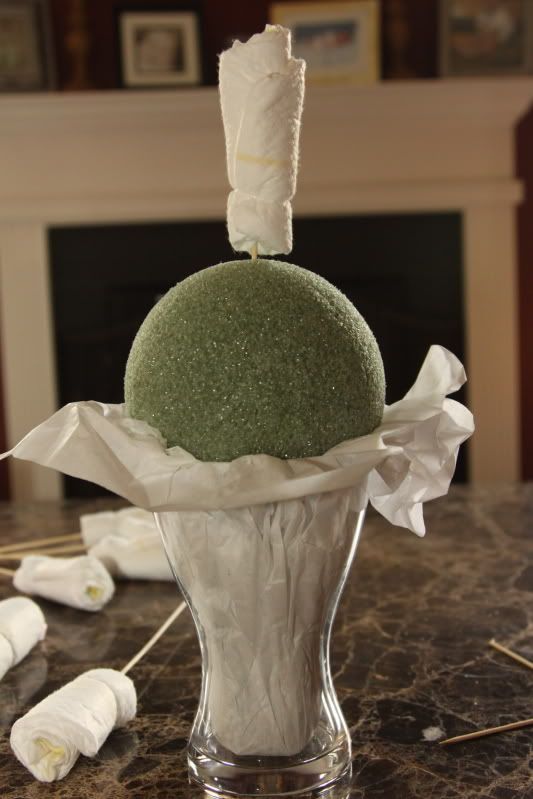 a white vase filled with a green ball on top of a table next to some cotton swabs