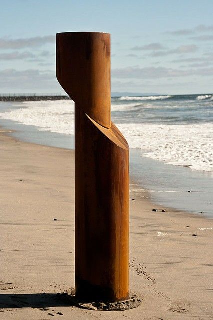 a sculpture on the beach with waves coming in from the water and sand behind it