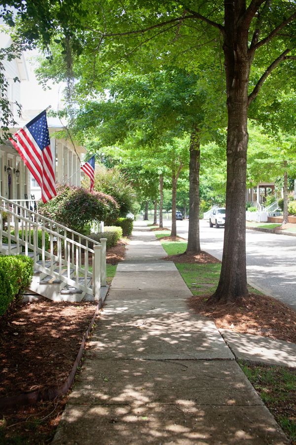 an american flag on the side of a tree lined sidewalk in front of a house