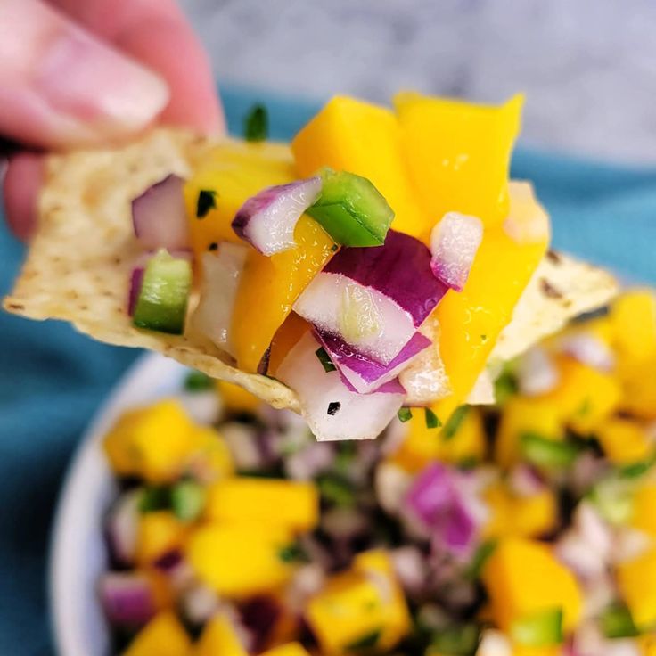 a person holding a tortilla chip over a bowl of fruit and veggies