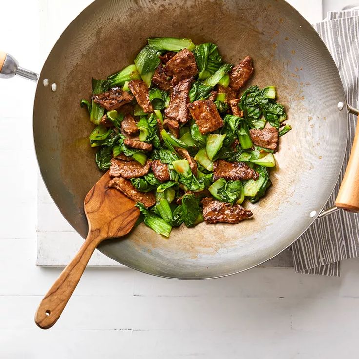 a wok filled with meat and vegetables on top of a white tablecloth next to utensils