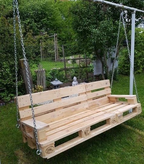 a wooden swing bench sitting on top of a lush green field