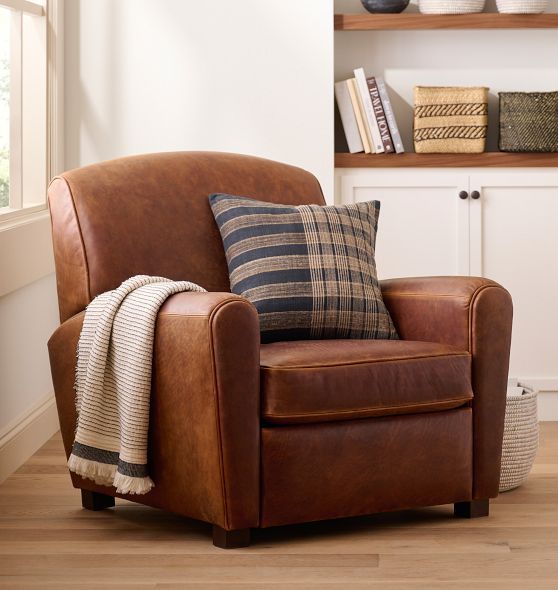 a brown chair sitting in front of a bookshelf filled with books and pillows