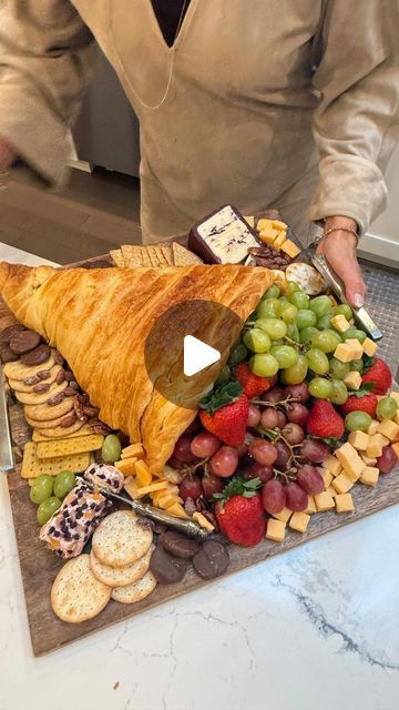 a man cutting up a large platter of fruit and crackers on top of a marble counter