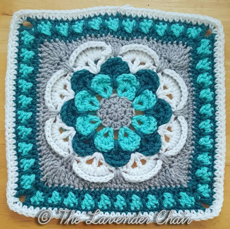 a crocheted square with a flower in the center on a wooden table top