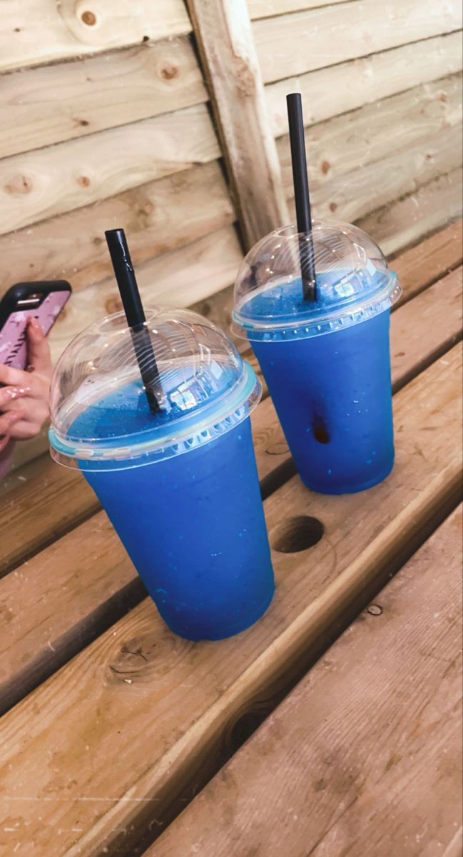 two blue drinks sitting on top of a wooden table next to each other with straws in them