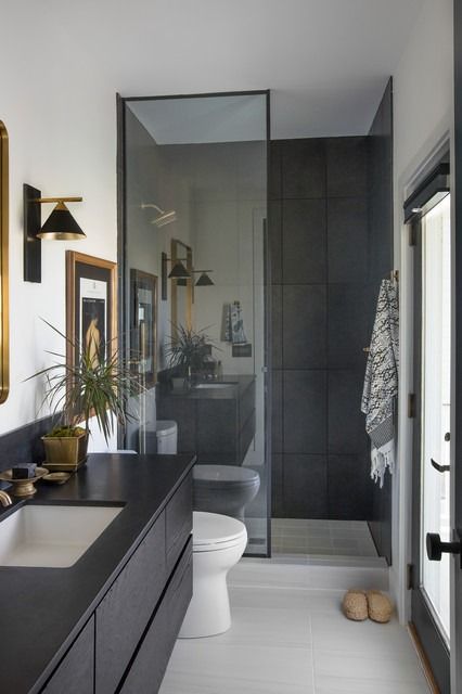 a bathroom with black counter tops and white flooring, along with a gold framed mirror on the wall