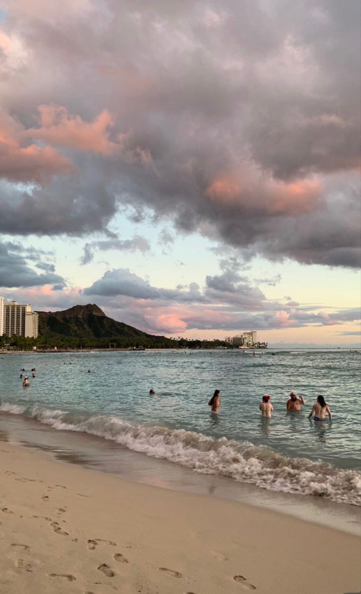 people are swimming in the ocean on a cloudy day at the beach with buildings in the background