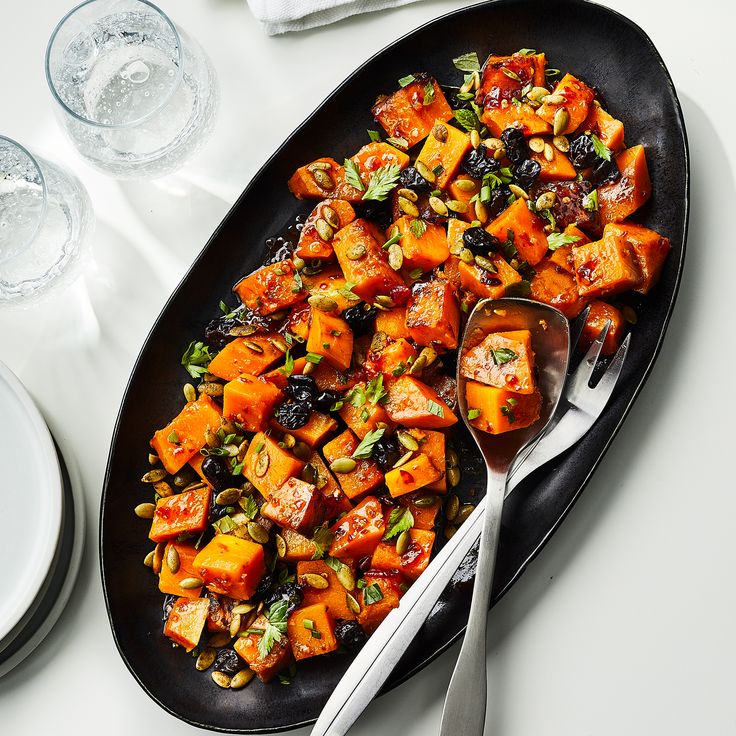 a black plate topped with lots of food next to two silver spoons on top of a white table