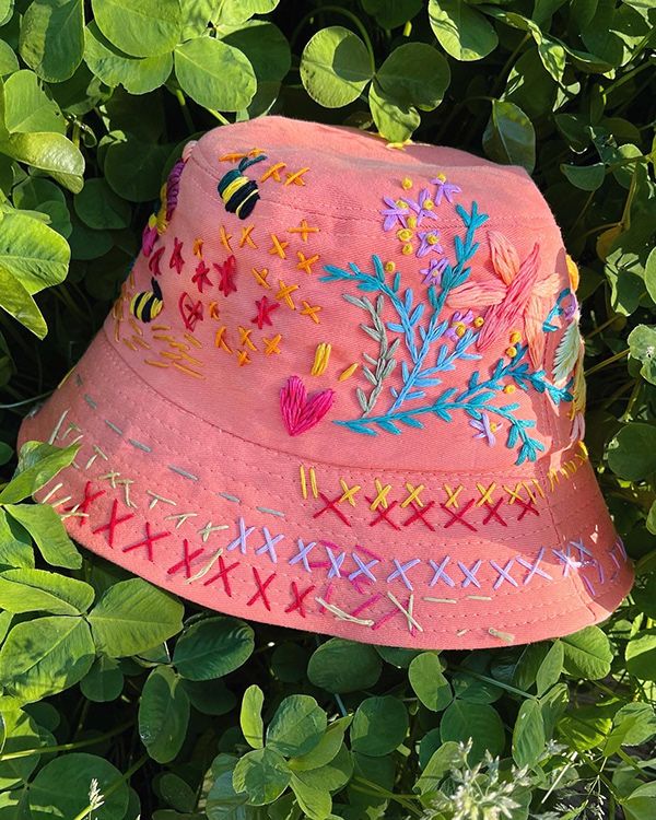 a pink hat with colorful embroidered designs on it sitting in the grass next to green leaves