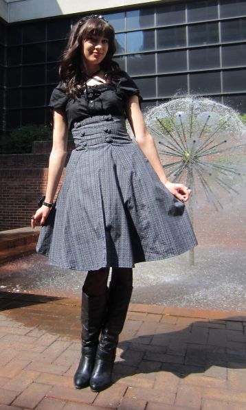 a woman standing in front of a fountain with an umbrella behind her back to protect herself from the sun