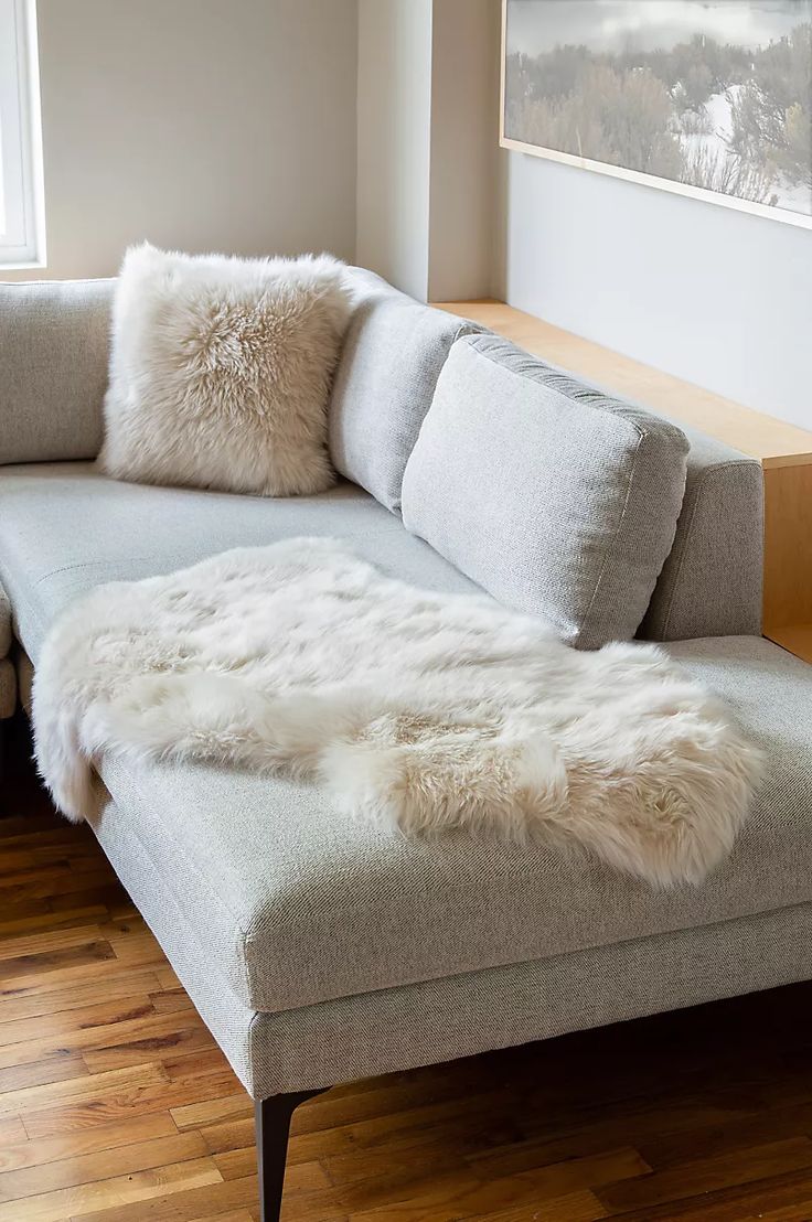 a couch with white fur on it in front of a window and wood flooring