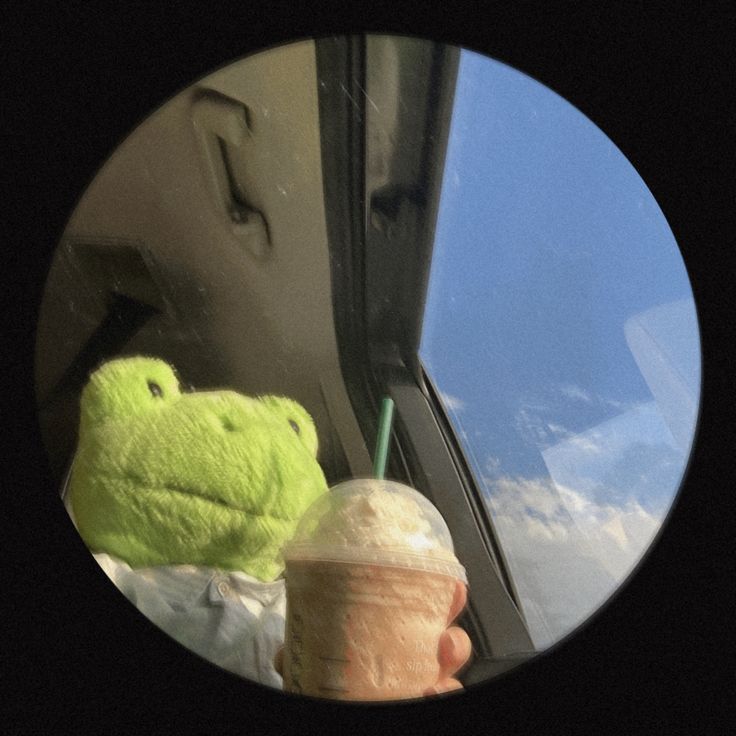 a person holding a drink in front of a window with a stuffed animal next to it