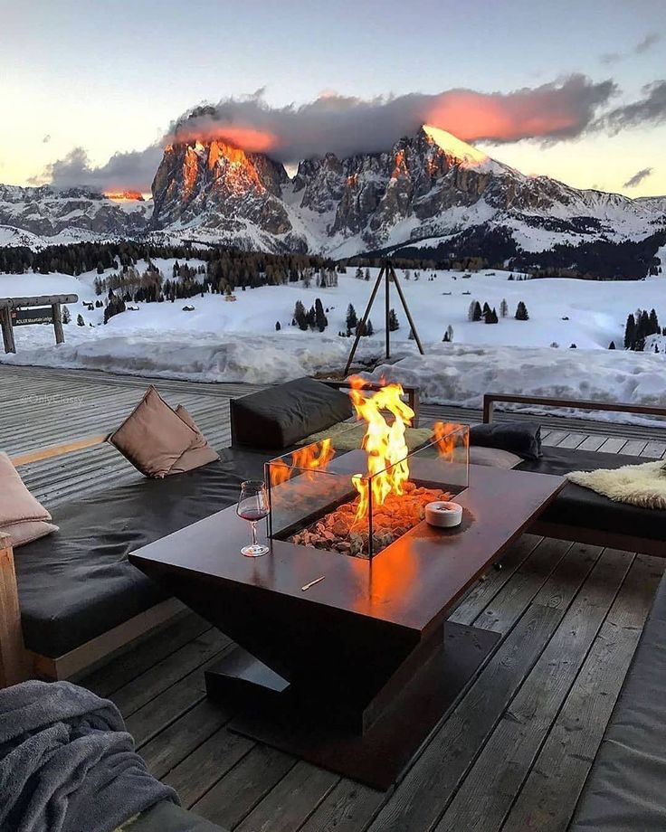 a fire pit sitting on top of a wooden deck next to snow covered mountain range