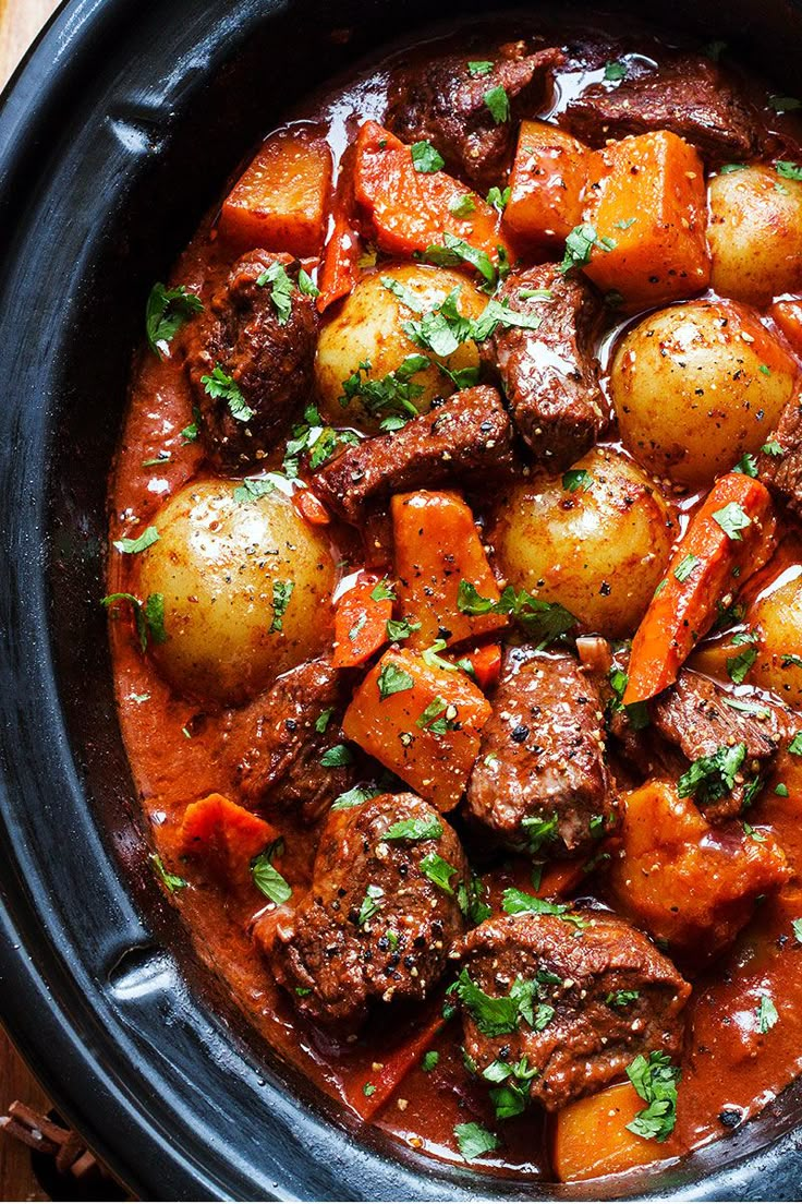 meat and potatoes stew in a black crock pot with parsley on the side