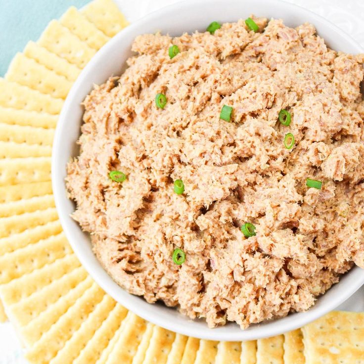 a white bowl filled with tuna dip surrounded by crackers