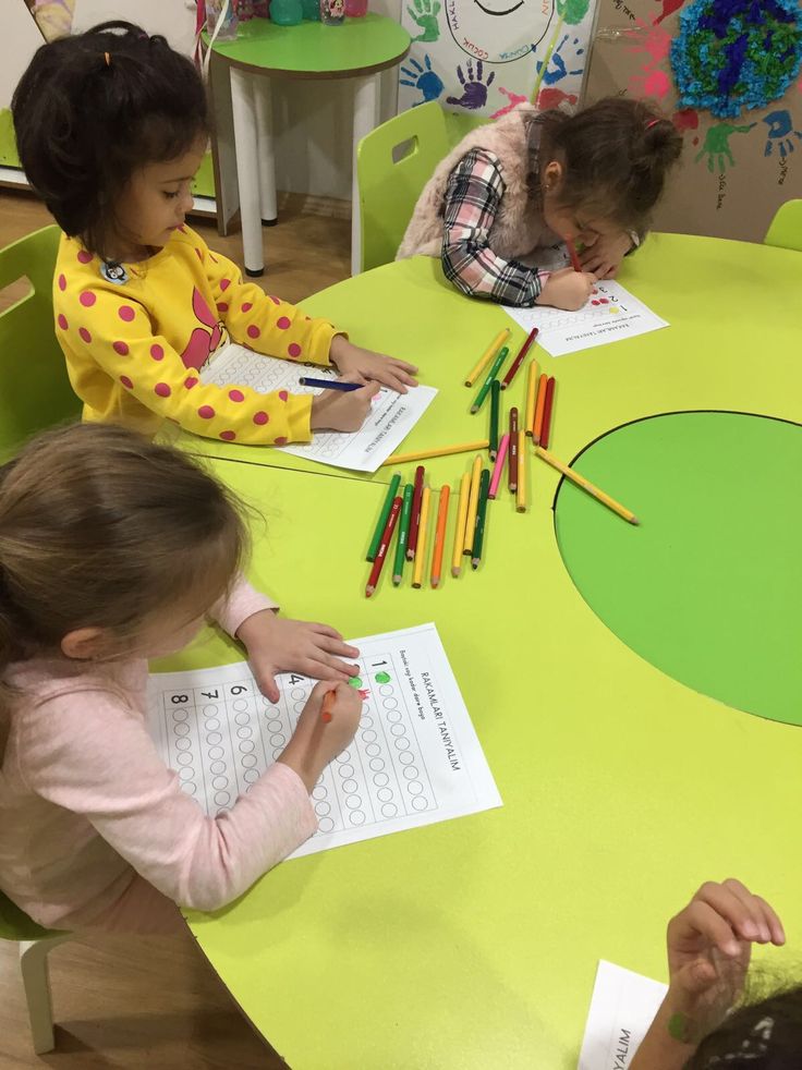 three children sitting at a table with colored crayons on the paper and writing