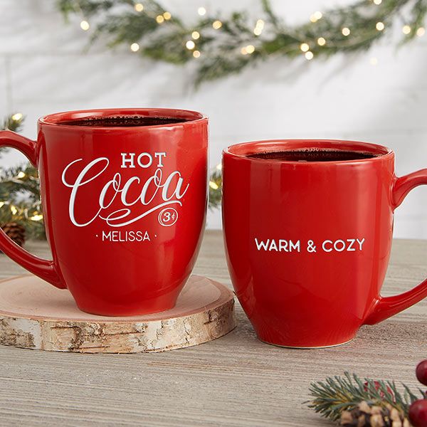 two red coffee mugs sitting on top of a wooden table next to christmas decorations