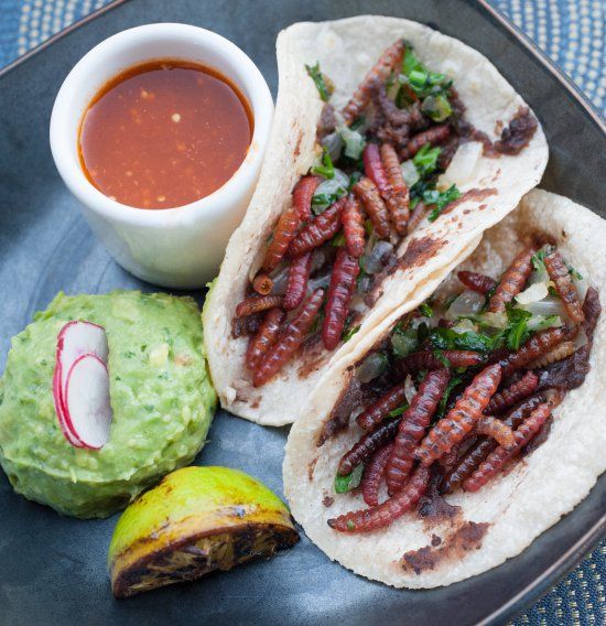 some tacos and guacamole are sitting on a plate next to an avocado