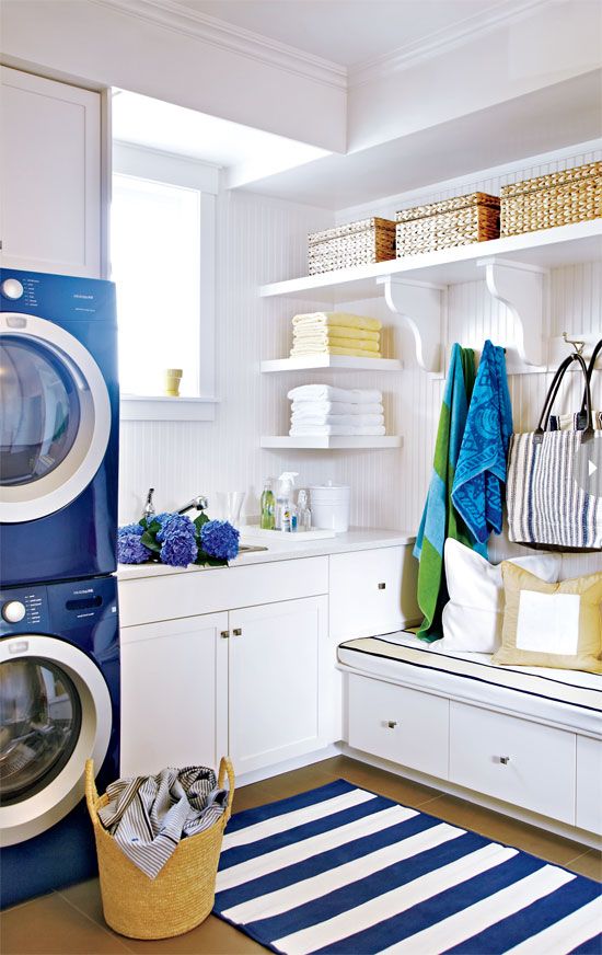 a washer and dryer in a small room with white cabinets, striped rugs and shelves