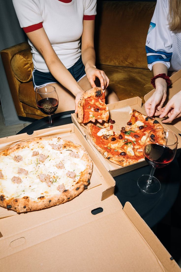 two people sitting at a table with pizza and wine