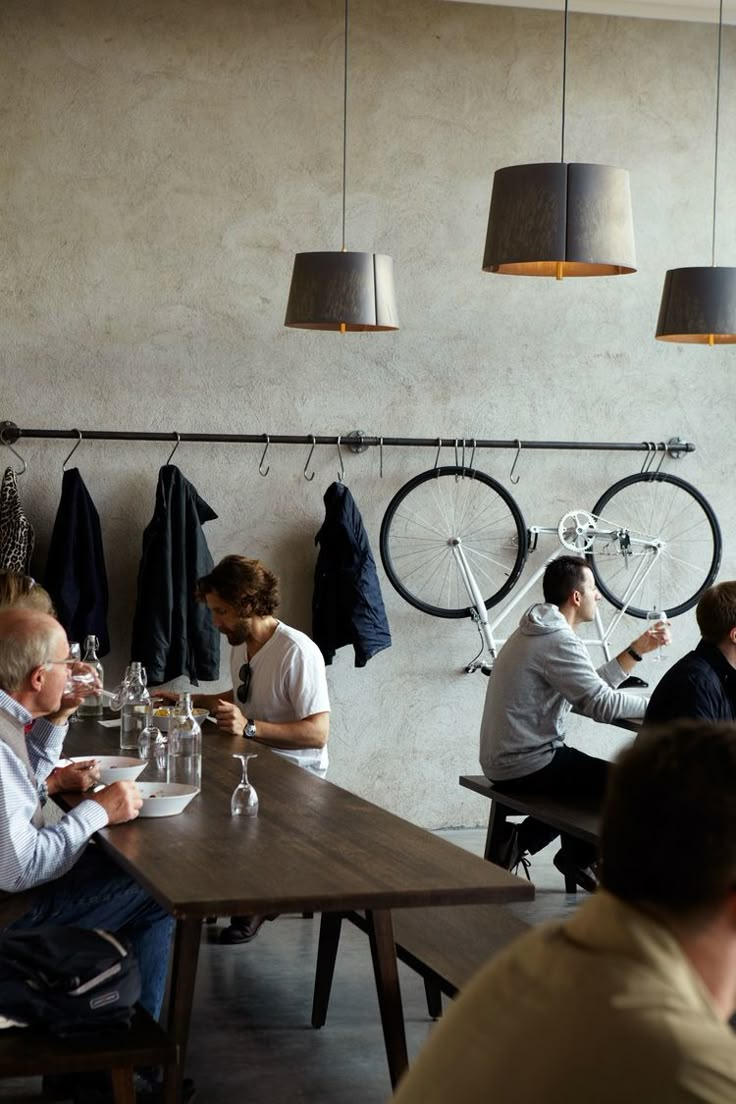 people sitting at tables in a restaurant with bikes hanging on the wall and lamps above them