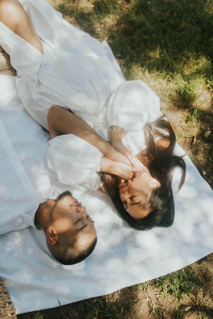 a man and woman laying on top of a blanket in the grass next to each other