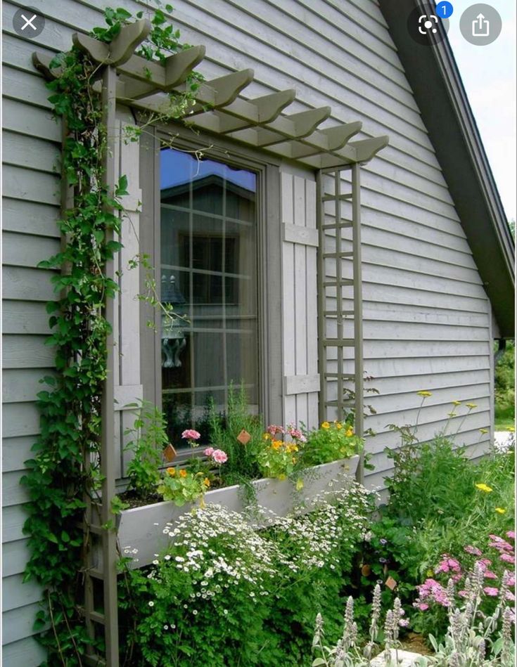 an open window on the side of a house covered in vines and flowers next to plants