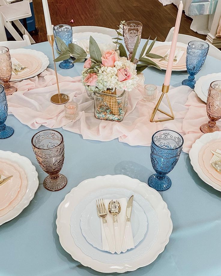 the table is set with blue and white plates, silverware, and pink flowers