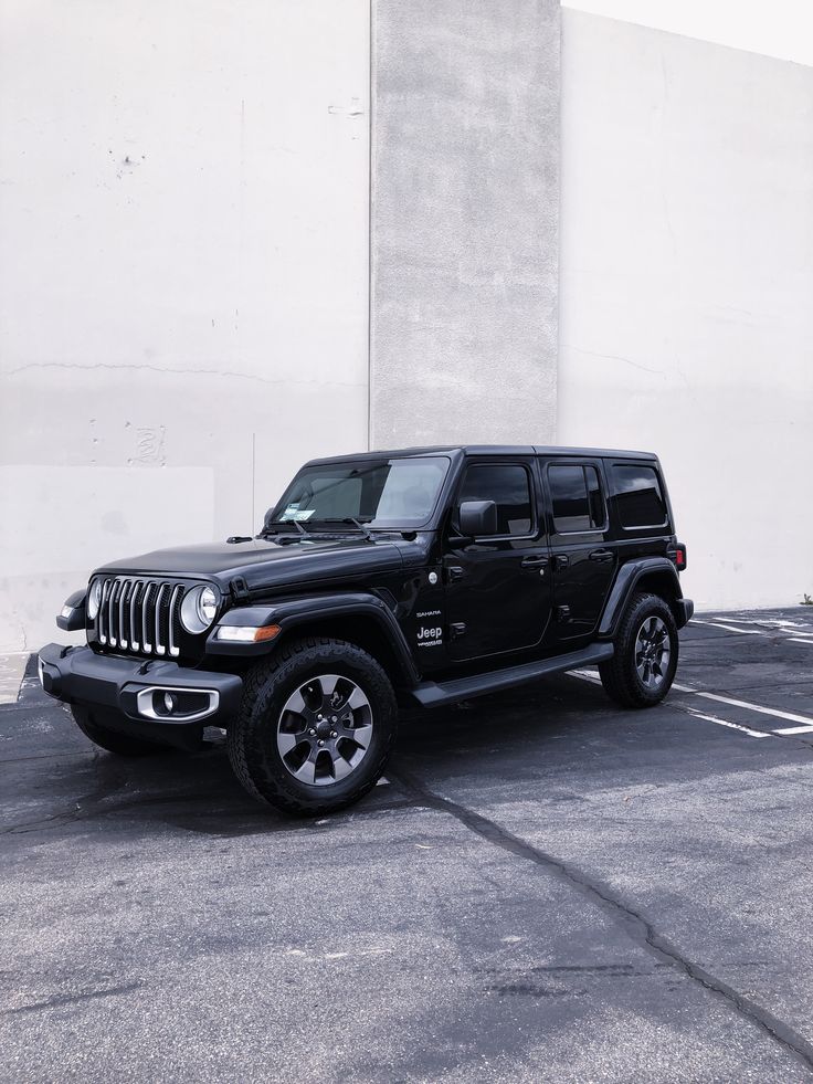 a black jeep parked in a parking lot next to a tall building with white walls