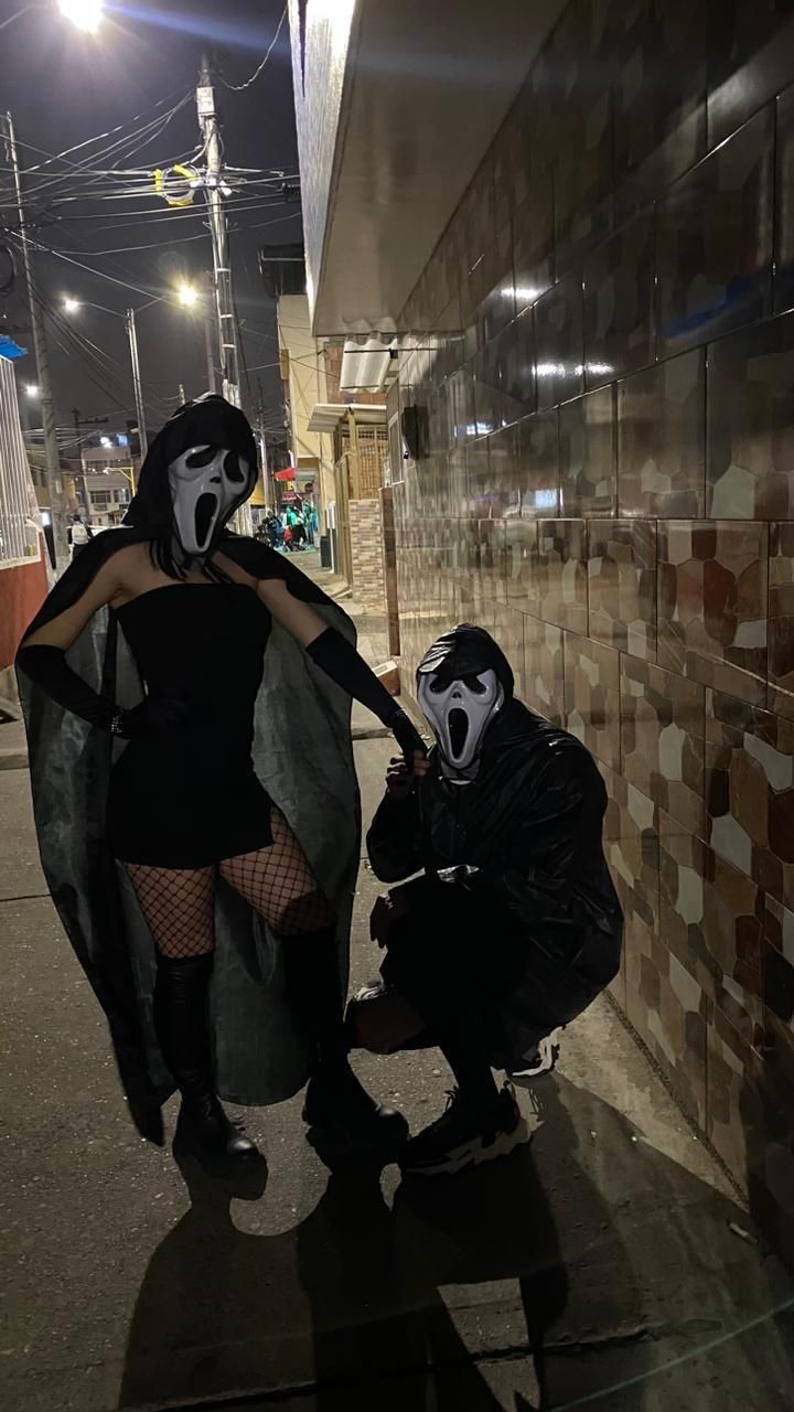 two people dressed up in costumes and masks on the street at night with one person wearing a mask