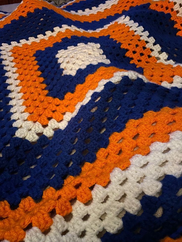 an orange, white and blue crocheted afghan is laying on top of a bed