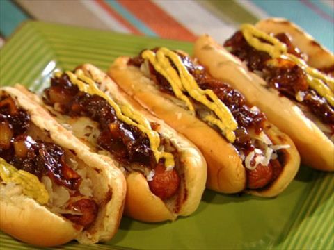 four hotdogs with chili and mustard on a green plate, ready to be eaten