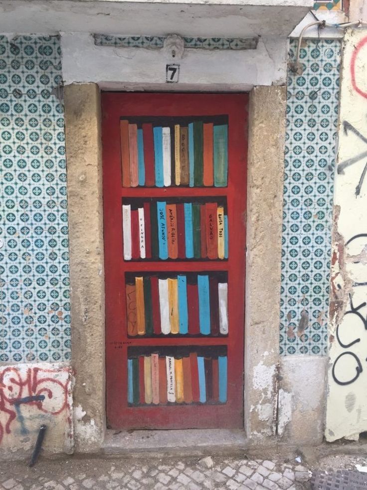 a red door with many books on it in front of a wall that has graffiti all over it