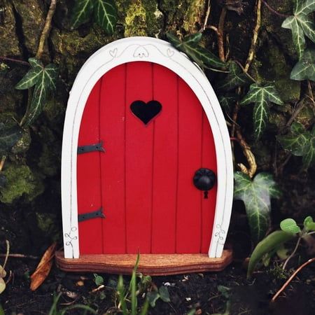 a red door with a heart on it in the middle of some grass and trees