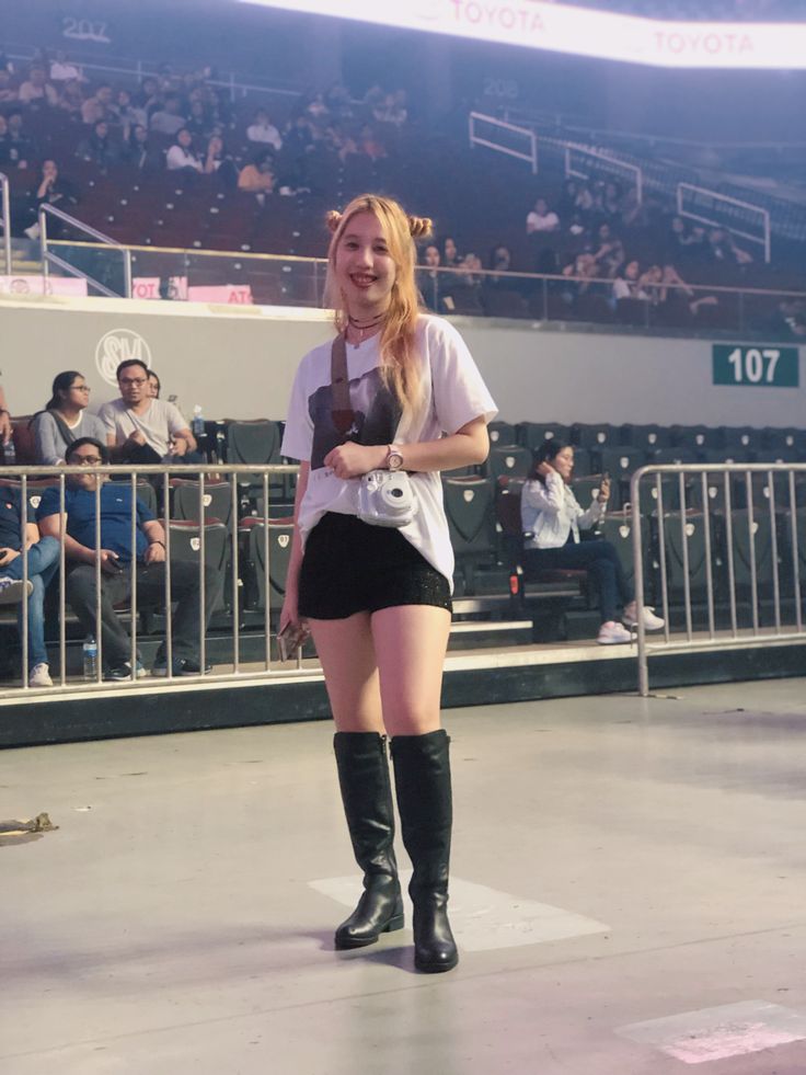 a woman standing in front of a crowd wearing knee high boots and holding a camera