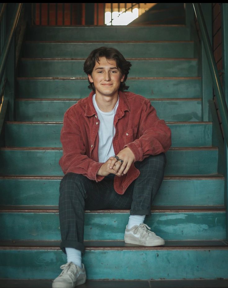 a young man sitting on top of a set of stairs with his hands in his pockets