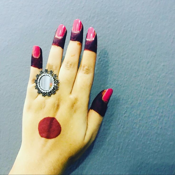 a woman's hand with red and black nail polish holding a ring on it