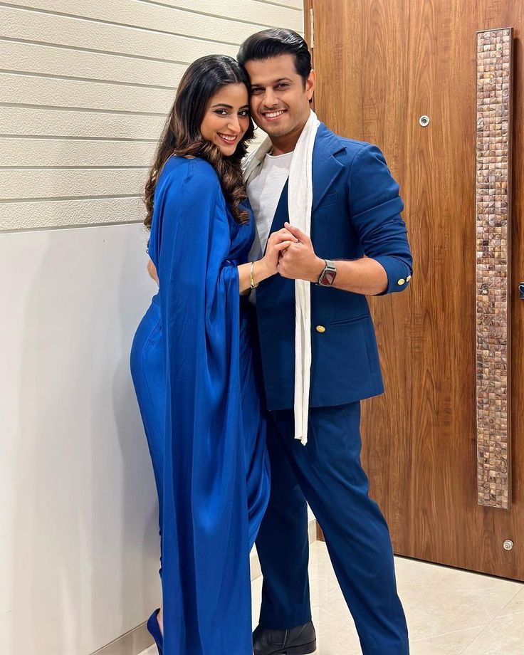 a man and woman standing next to each other in front of a door wearing blue outfits