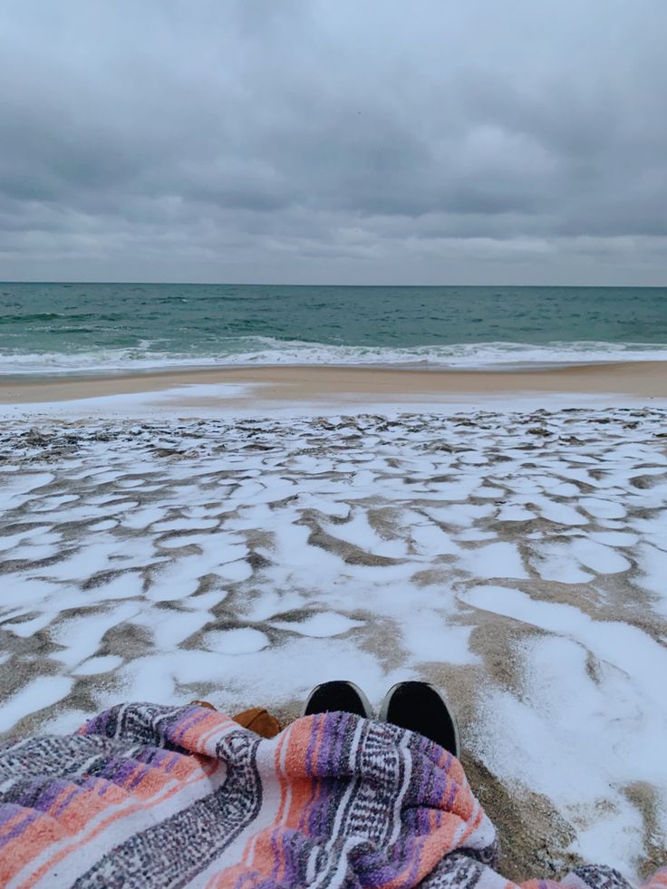 someone is laying down on the beach covered in blankets and looking out at the ocean