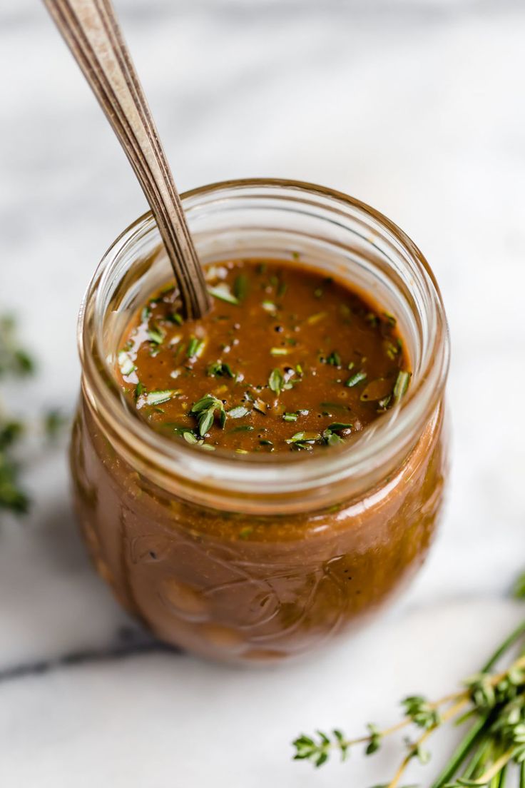 a jar filled with sauce sitting on top of a table next to some green herbs