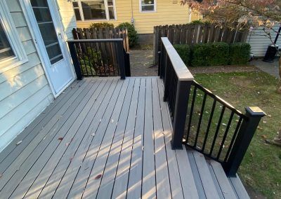 a wooden deck in front of a yellow house with black railing and handrails