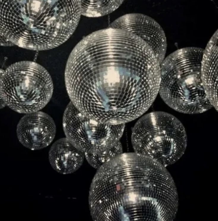 many disco balls hanging from the ceiling in front of a black background with white lights