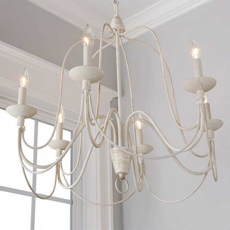 a white chandelier hanging from the ceiling in a room with windows and curtains