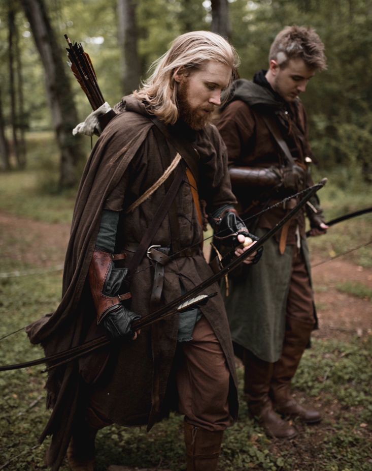 two men dressed in medieval costumes are walking through the woods