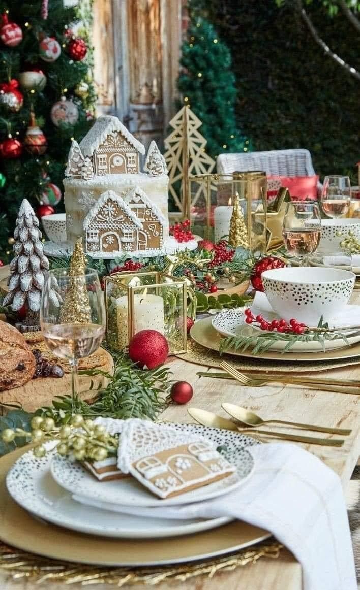 a table set for christmas dinner with plates, silverware and gold place settings in front of a christmas tree